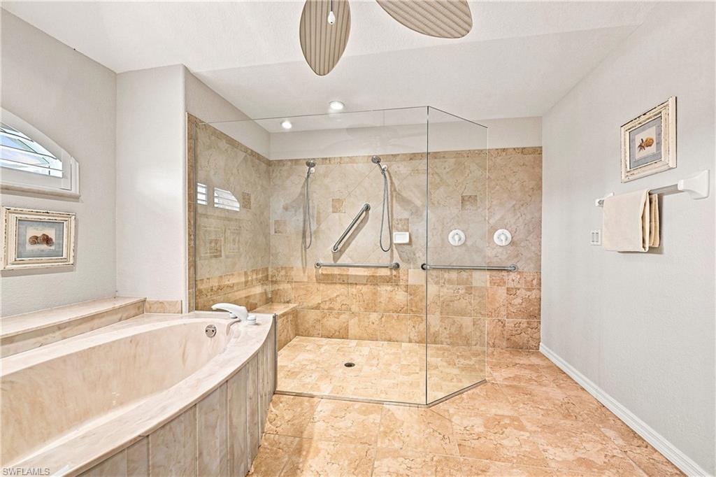 Spa-inspired primary bathroom featuring a frameless glass-enclosed walk-in shower with dual showerheads and body jets, heated floor, and travertine tile surround