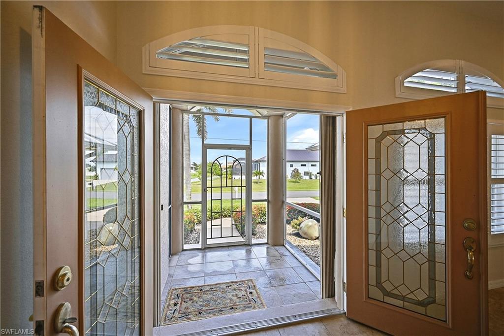 Elegant foyer showcasing leaded glass French doors with geometric patterning, transom windows with arched detailing, and stone tile flooring