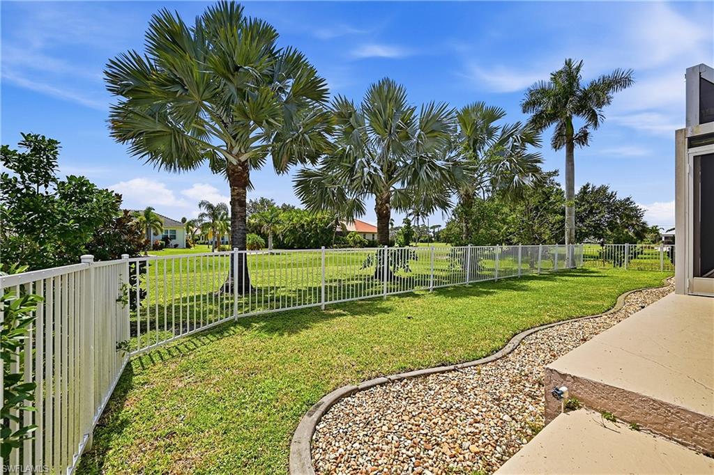 Expansive fenced backyard with mature palm trees, manicured lawn, decorative rock landscaping, and aluminum fencing for play area or dog run