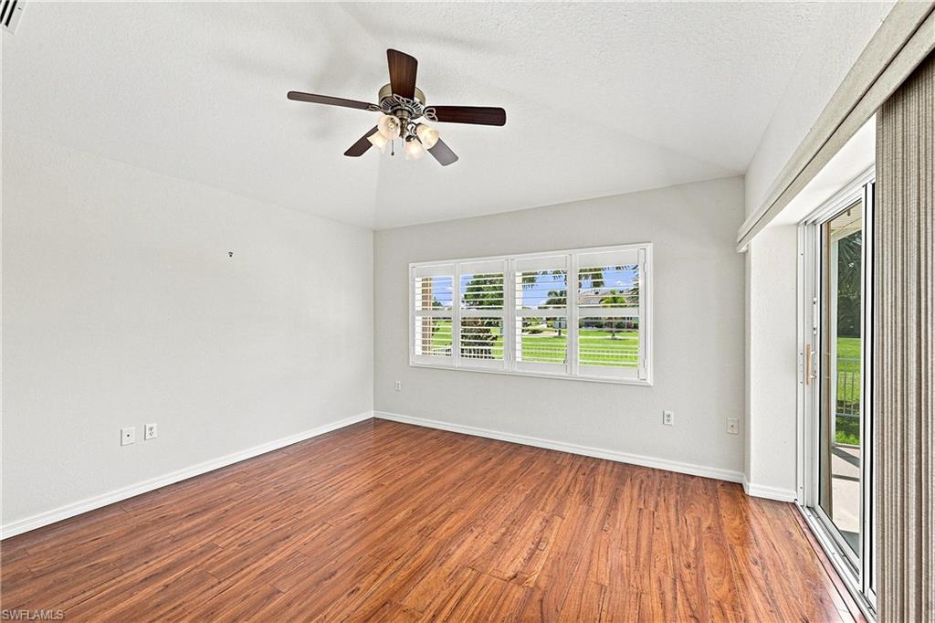 Bright, light-filled room featuring wood-finish flooring, ceiling fan with integrated lighting, multi-pane windows framing natural outdoor scenery