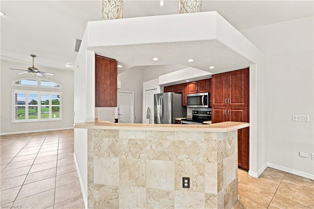 Open-concept kitchen and dining area featuring rich wood-finish cabinetry, stainless steel appliances, and a natural stone-finish island with breakfast bar