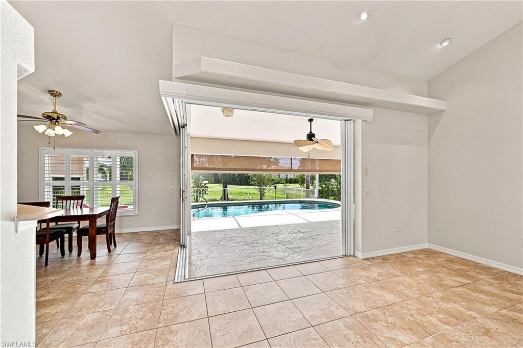 Spacious living room with tile flooring and multi-panel 90-degree 8 ft high sliding glass doors opening to the outdoor entertaining area. Under truss patio area has protective retractable kevlar hurricane screen.