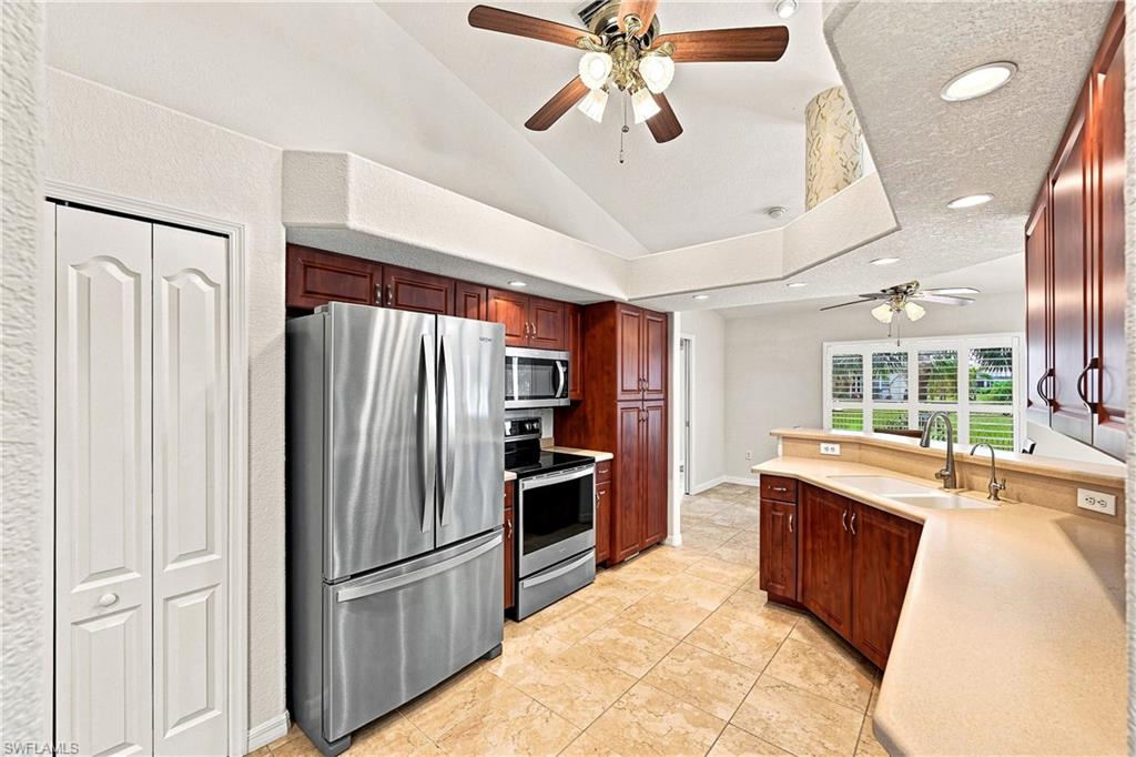 Elegant kitchen featuring rich cherry cabinetry, stainless steel French-door refrigerator and matching appliances, tile flooring, quartz countertops, an island with seating, ceiling fan with recessed lighting, and abundant natural light from multiple windows