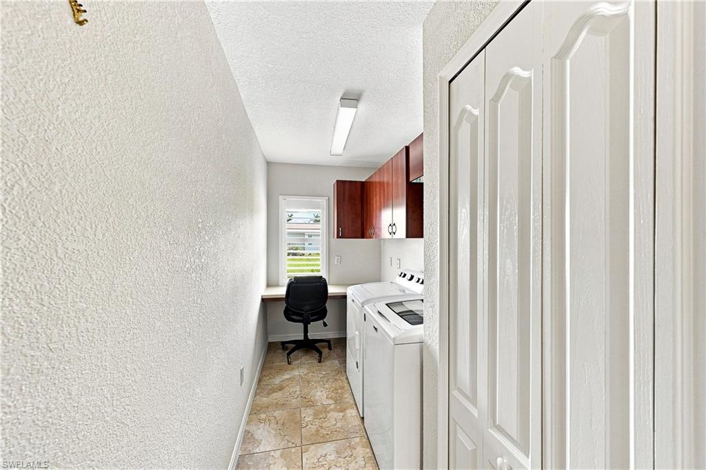 Efficient laundry room layout featuring tile flooring, desk area for folding clothes, wood paneled cabinets, and white panel pantry doors