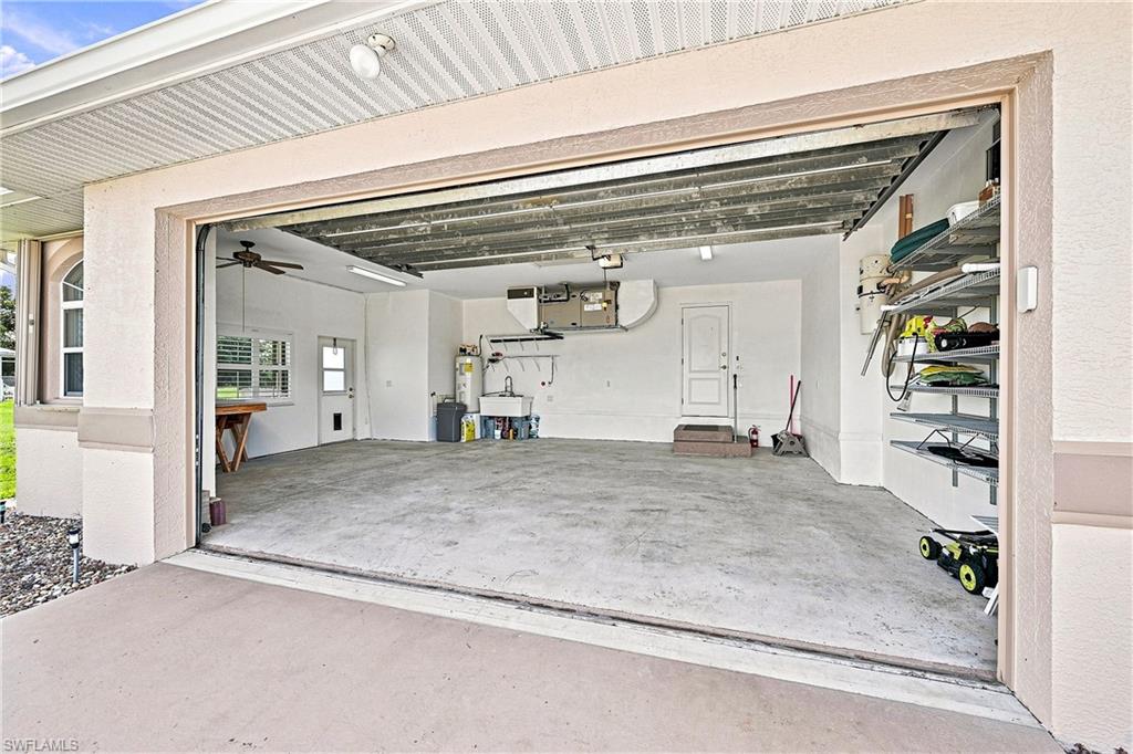 Spacious garage featuring a ceiling fan, built-in utility sink, multiple windows with blinds, an interior door, exterior side door, and wall-mounted shelving