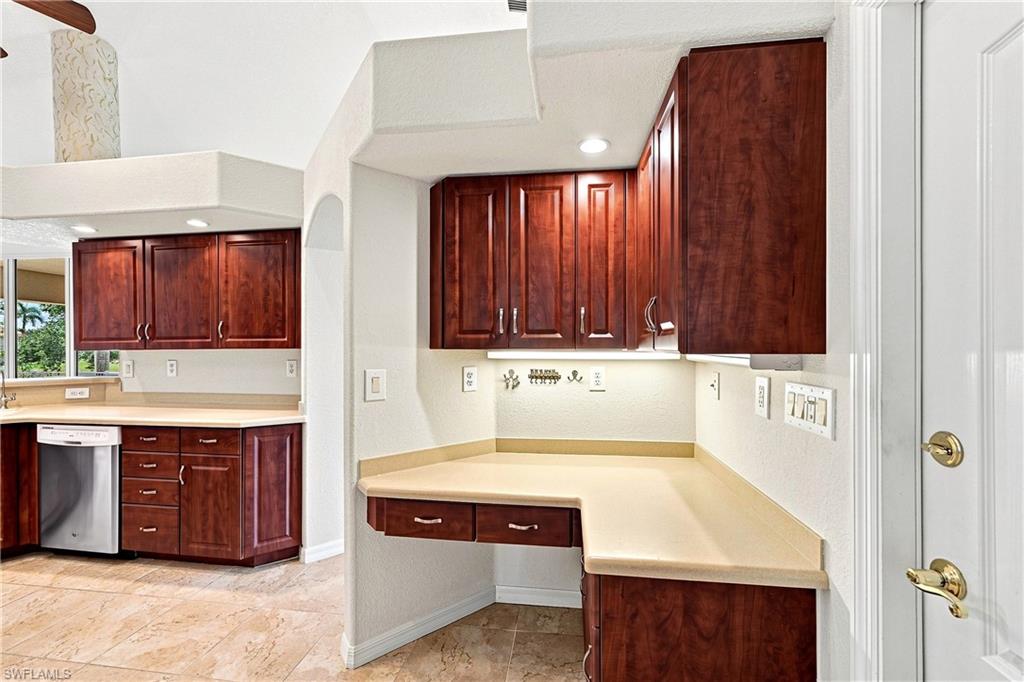 Elegant kitchen workspace featuring rich cherry wood cabinetry, cream-colored countertops, stainless steel appliances, recessed lighting, and a generous built-in desk area with additional storage drawers