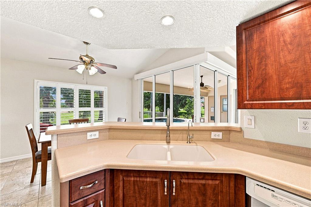 Chef's kitchen featuring a curved island with rich wood cabinetry, dual undermount sinks with polished nickel fixtures, and expansive cream-colored countertops