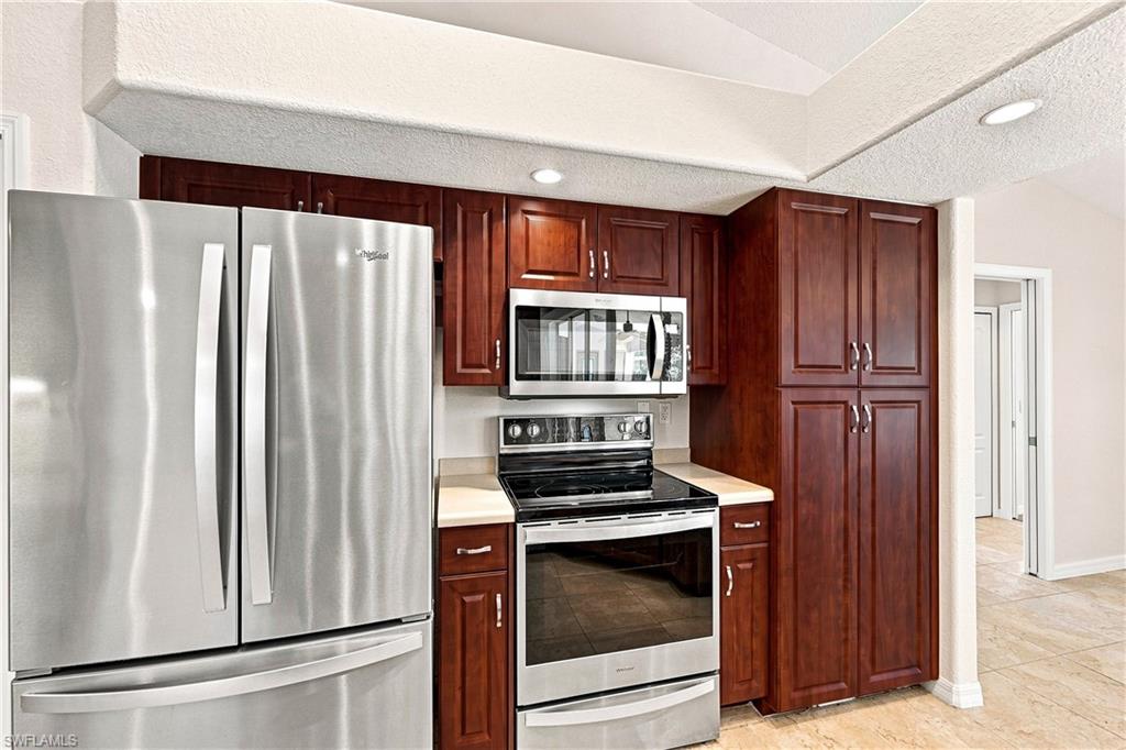 Modern kitchen featuring rich wood cabinetry with brushed nickel hardware, stainless steel appliances including a French-door refrigerator, electric range with microwave, and stone countertops