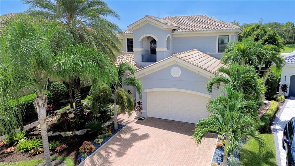 Tiled roof home featuring a paver driveway, an attached two-car garage, and premium landscaping with palm trees, and landscape lighting