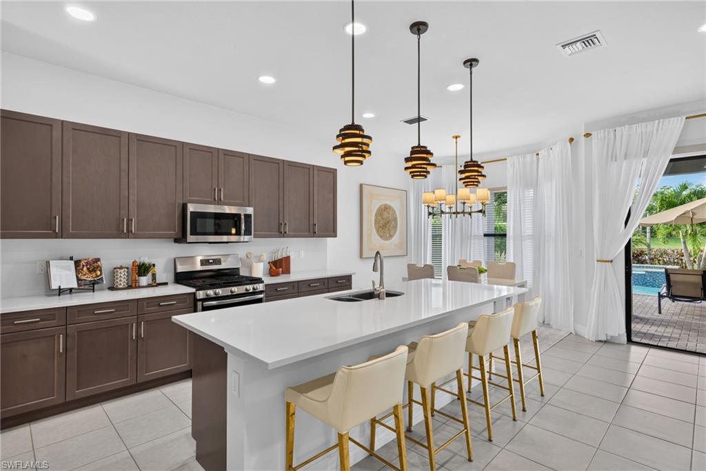 Kitchen featuring dark wood-finish cabinetry, white countertops, stainless steel appliances, and a central island with an integrated sink