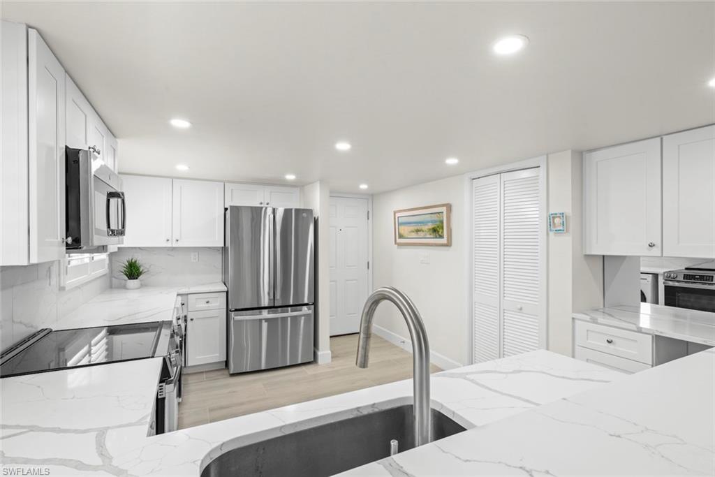 Contemporary kitchen featuring white cabinetry, stainless steel appliances, a tile backsplash, and light-toned wood-finish flooring
