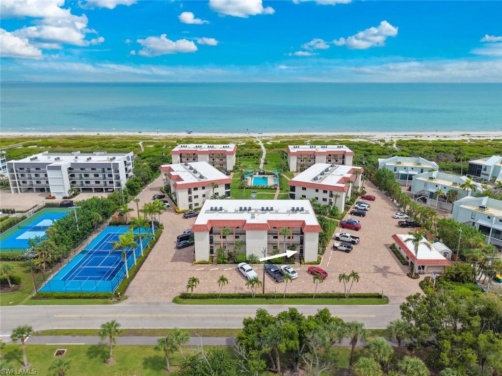 Coastal complex featuring multiple multi-story buildings, a paved parking area, and a blue tennis court