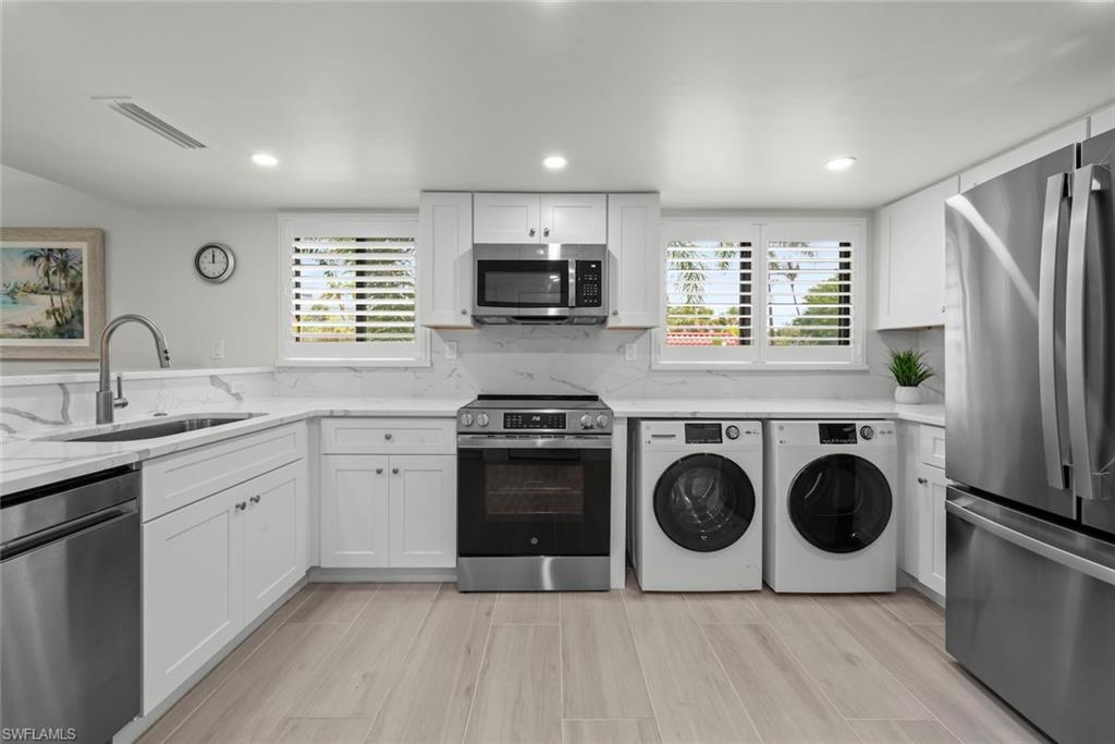 Modern kitchen featuring white shaker cabinetry, stainless steel appliances, marble-look countertops, and plank tile flooring