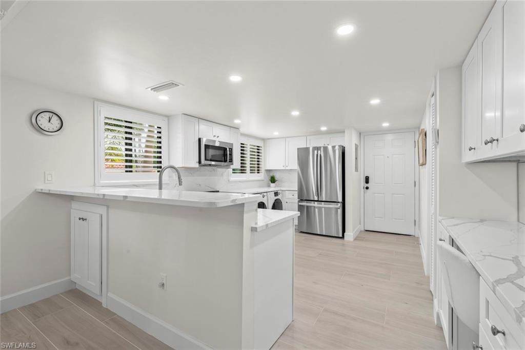 Modern kitchen featuring white cabinetry, stainless steel appliances, marble-look countertops, and recessed lighting
