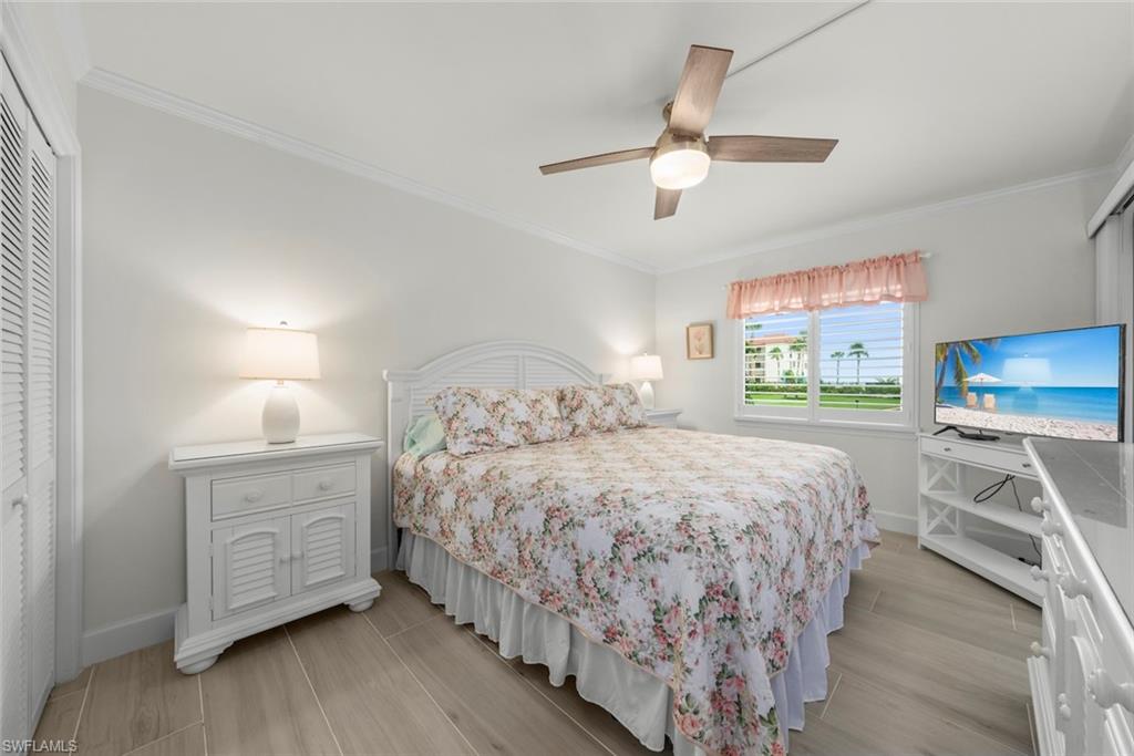 Bedroom featuring wood-finish flooring, a ceiling fan with integrated lighting, a window with plantation shutters, and a louvered bi-fold closet door