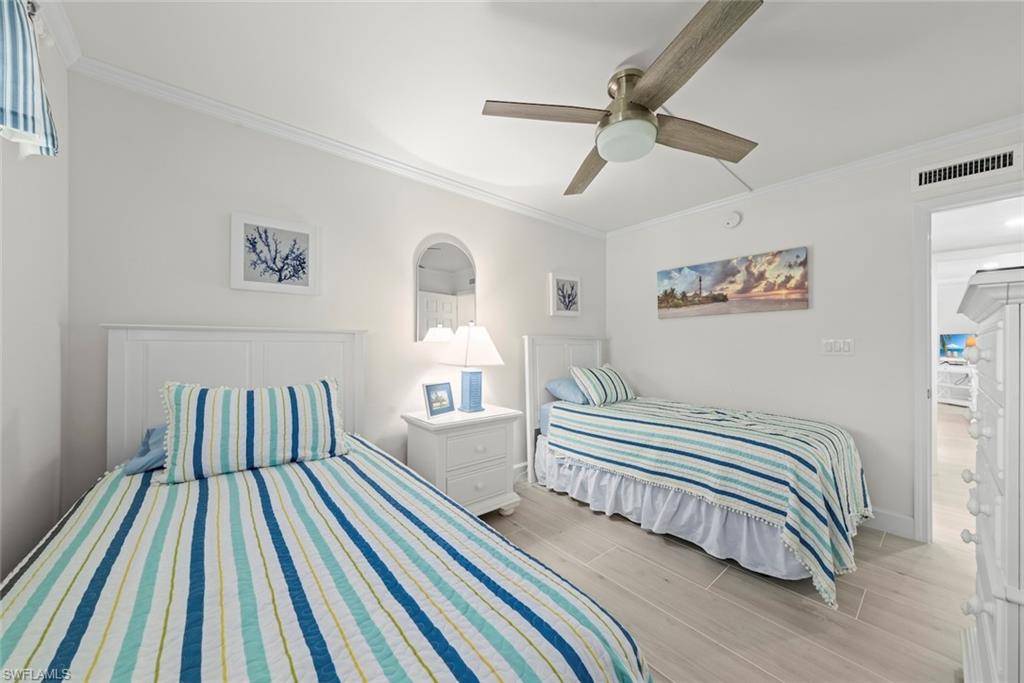 Bright room featuring two white headboards, wood-finish flooring, an overhead ceiling fan, and crown molding