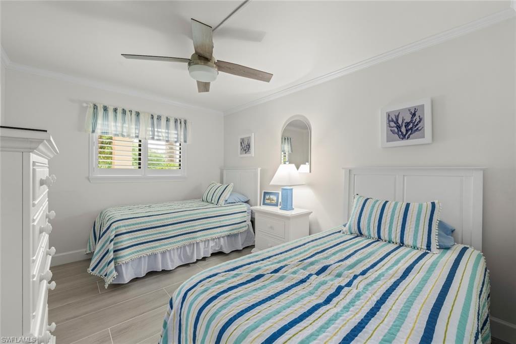 Bedroom featuring two single beds, wood-finish flooring, a ceiling fan, crown molding, and a window with plantation shutters