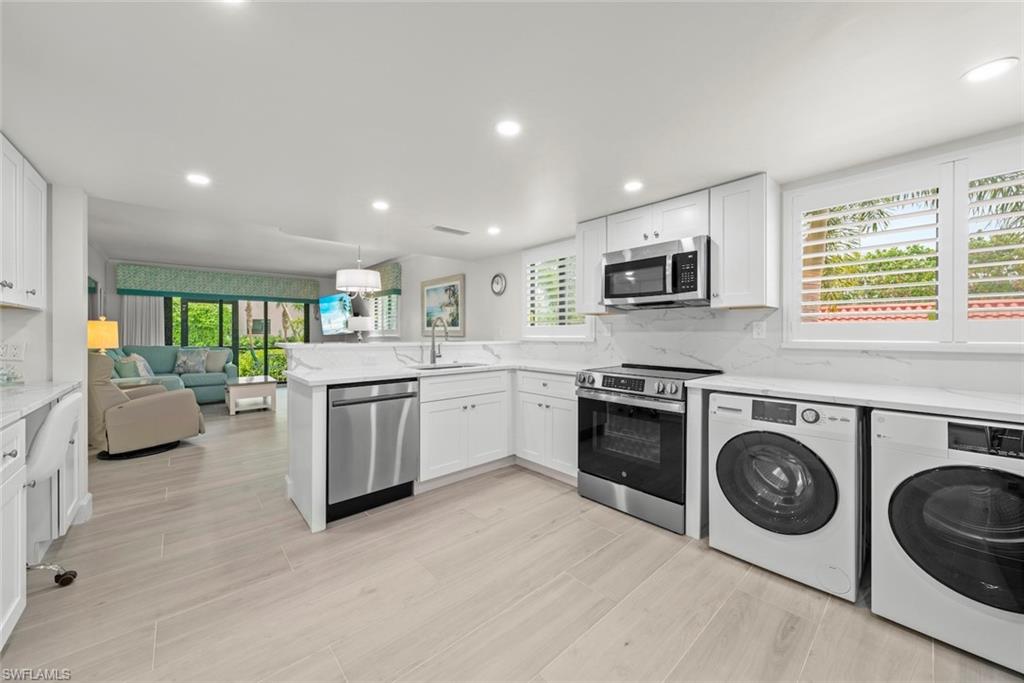 Gourmet kitchen featuring stainless steel appliances, white cabinetry, integrated laundry machines, and light wood-finish flooring