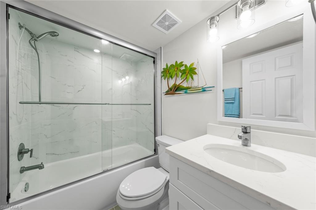 Bathroom featuring a tub/shower combination with sliding glass doors, white tiled surround, and brushed nickel fixtures