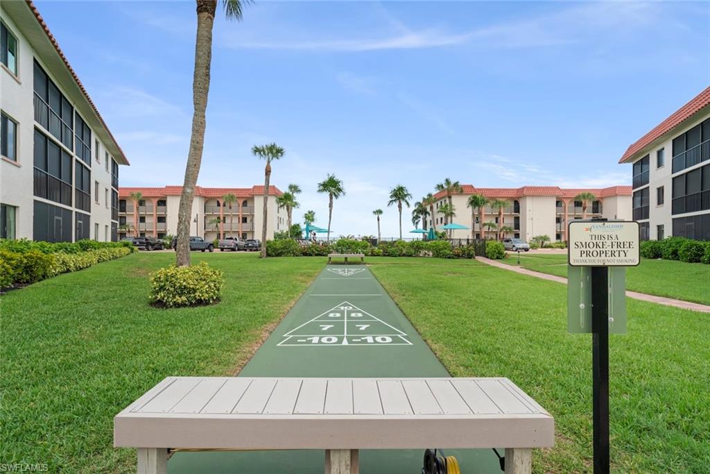 Manicured green space featuring a shuffleboard court with scoring lines, surrounded by lush landscaping and palm trees