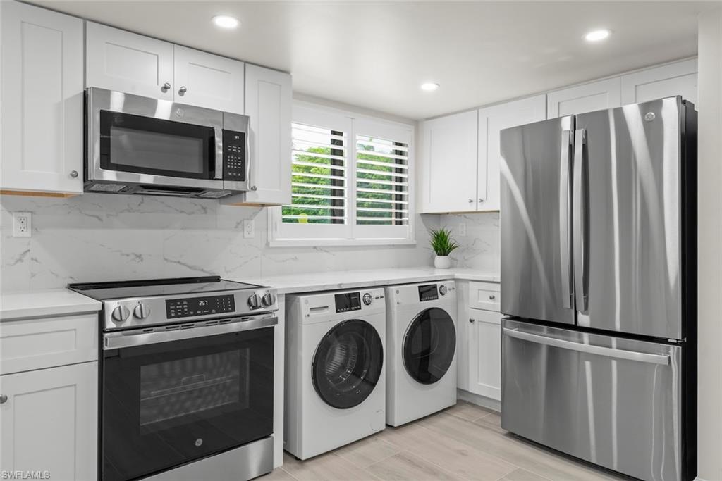 Kitchen featuring white shaker cabinetry, stainless steel appliances, marble-look backsplash, white countertops, and wood-finish flooring