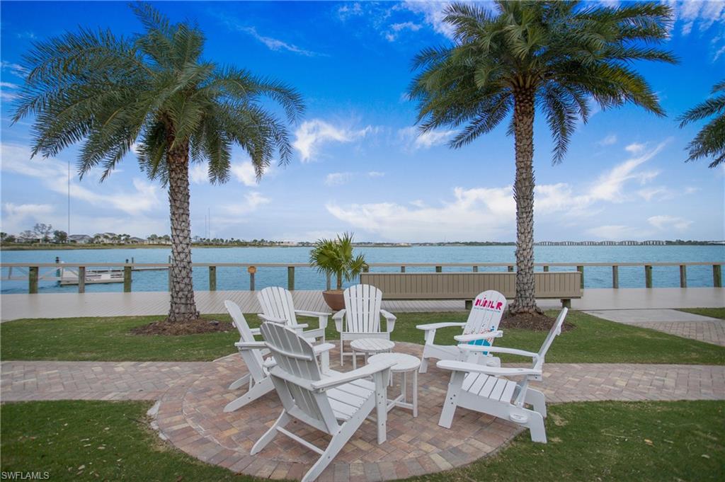 Lakefront paver patio with Adirondack seating and palm trees, overlooking the community lake and boardwalk dock.