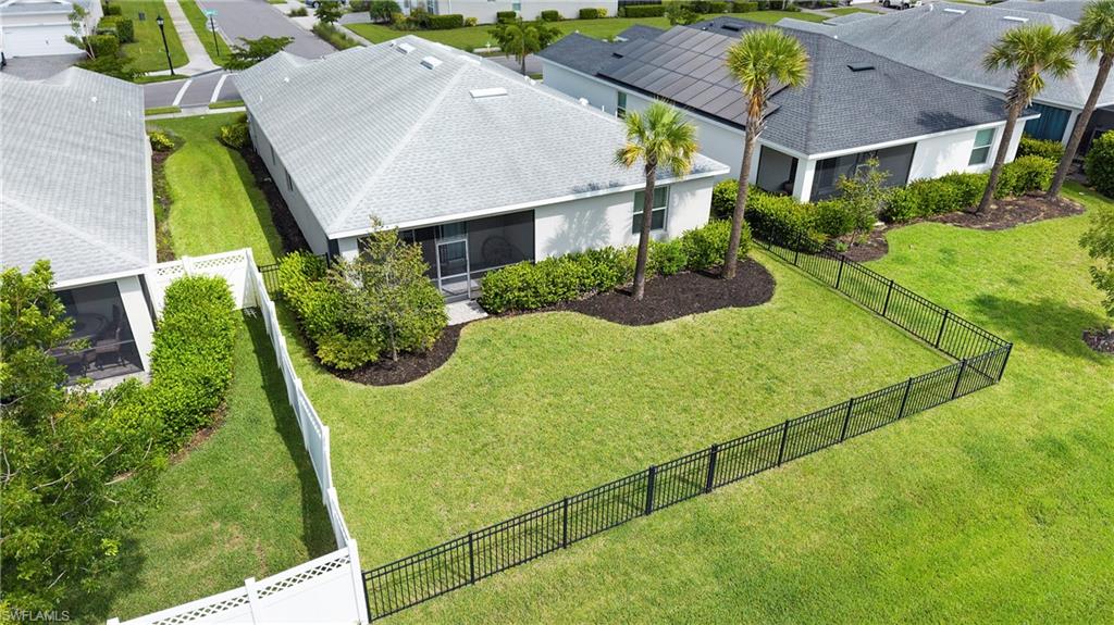 Expansive backyard featuring a manicured lawn, a black metal fence, and mature landscaping