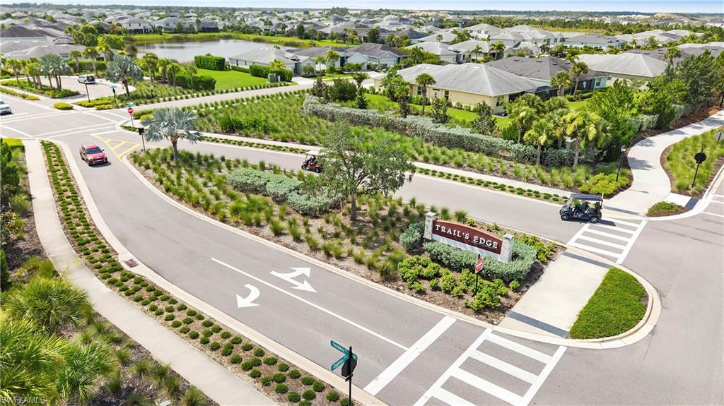 Aerial view of the Trail’s Edge community entrance with a landscaped monument sign, golf cart friendly streets, sidewalks and walking paths, and a community lake.