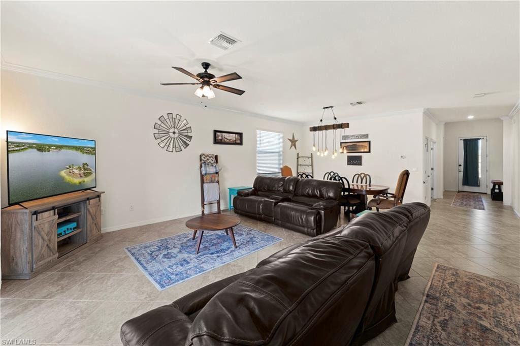 Open-concept great room with tile flooring, crown molding, and a lighted ceiling fan. Sightlines flow from the living area into the dining space and kitchen.