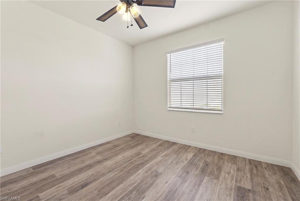 Room featuring wood-finish flooring, white baseboards, a window with horizontal blinds, and a ceiling fan with light fixture