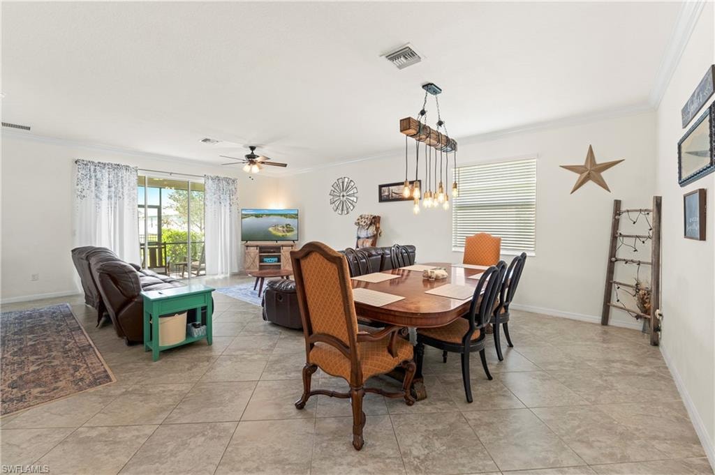 Open-concept living and dining area featuring neutral tile flooring, a multi-bulb chandelier, and crown molding