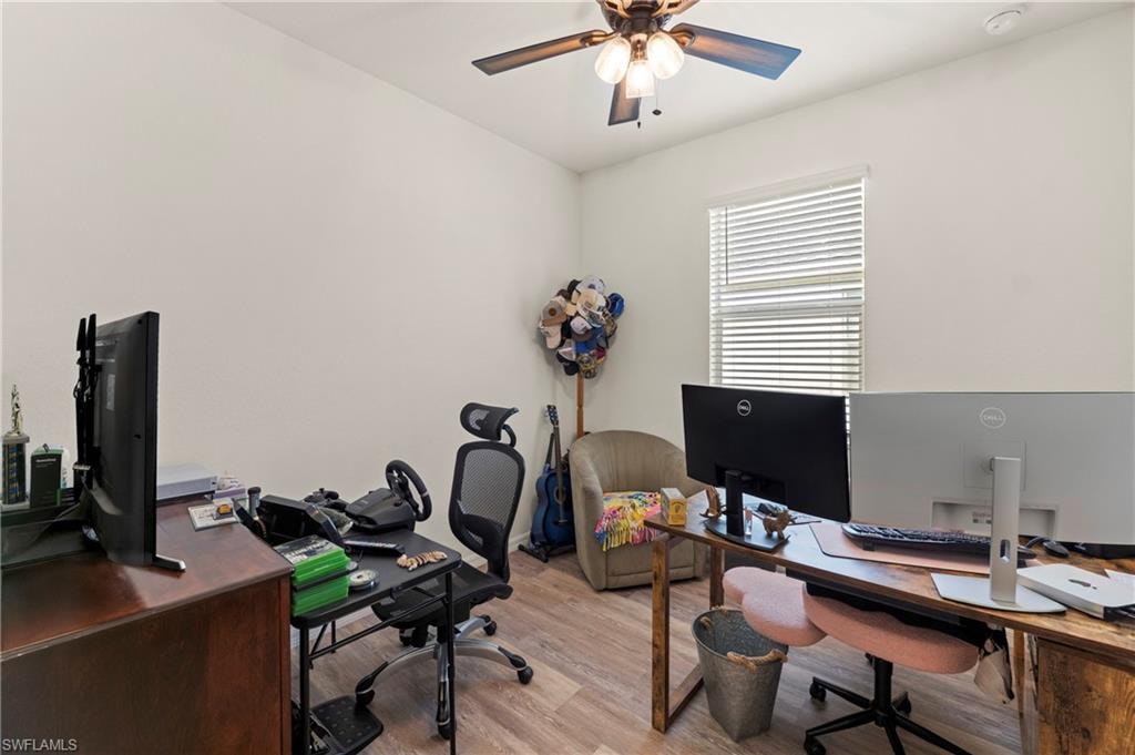 Flexible room set up as a home office with luxury vinyl plank flooring, a lighted ceiling fan, and a window with blinds. Works as a home office, den, or additional bedroom.