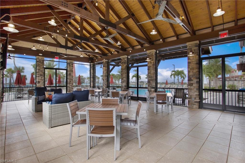 Open-air gathering pavilion with a stone fireplace, mounted TV, and lounge seating under a vaulted timber ceiling. Poolside and lakefront setting.