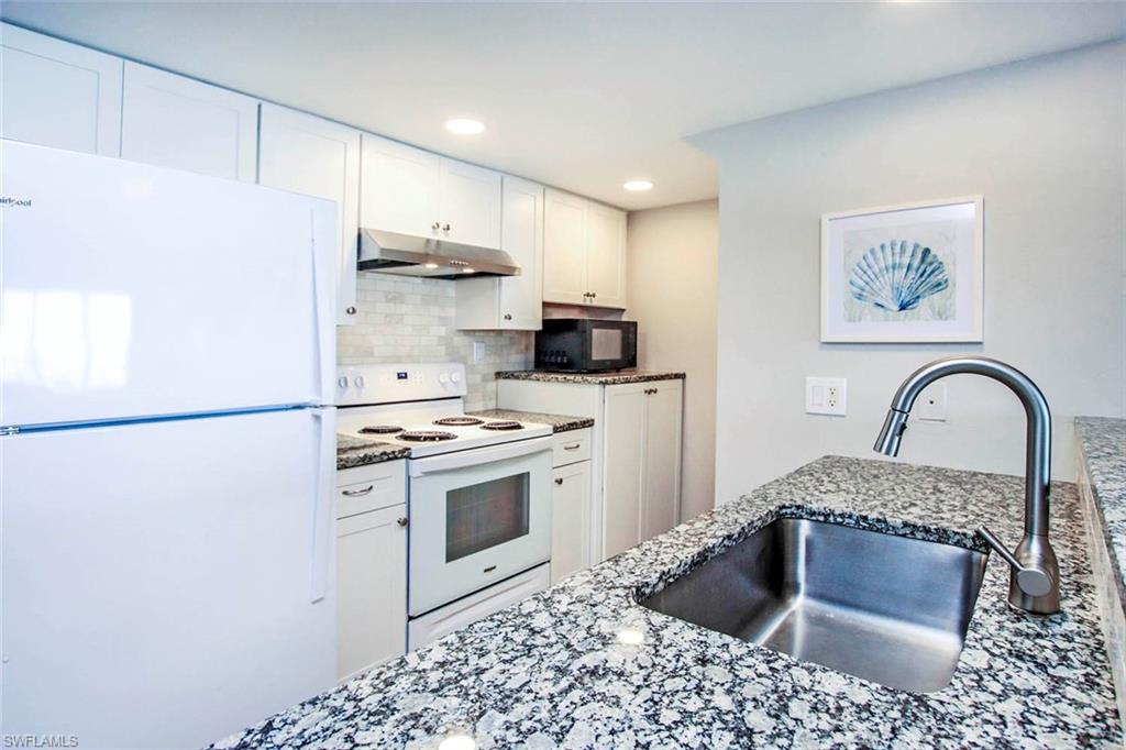 Kitchen features recessed lighting, dark stone countertops & stainless sink.