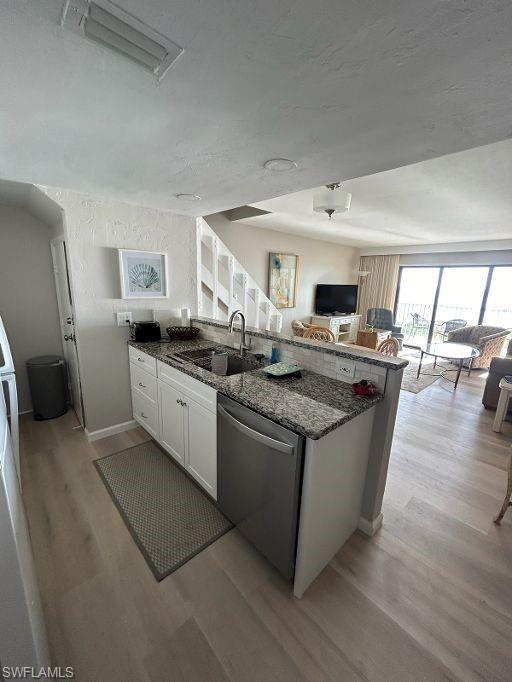Kitchen with stainless steel dishwasher, open floor plan, light wood-style floors, and dark stone counters