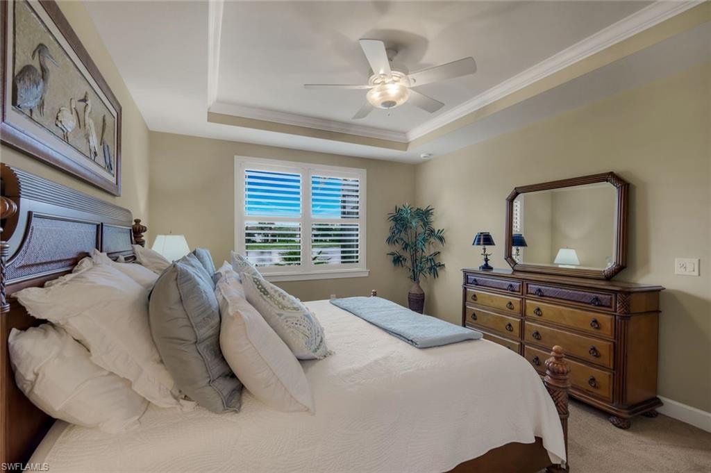 Tray ceiling, ceiling fan with light fixture, window with plantation shutters, wood-finish headboard, and wood-finish dresser
