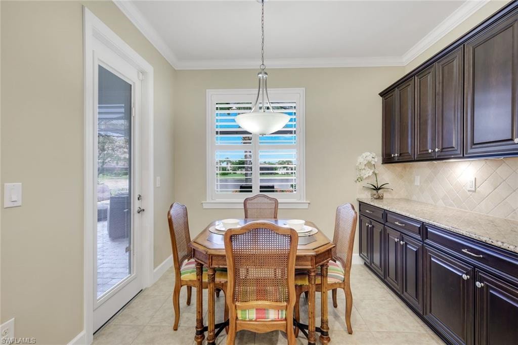 Wood-finish cabinetry with silver hardware, light-toned countertop, diagonal tile backsplash, under-cabinet lighting, and a full-light exterior door