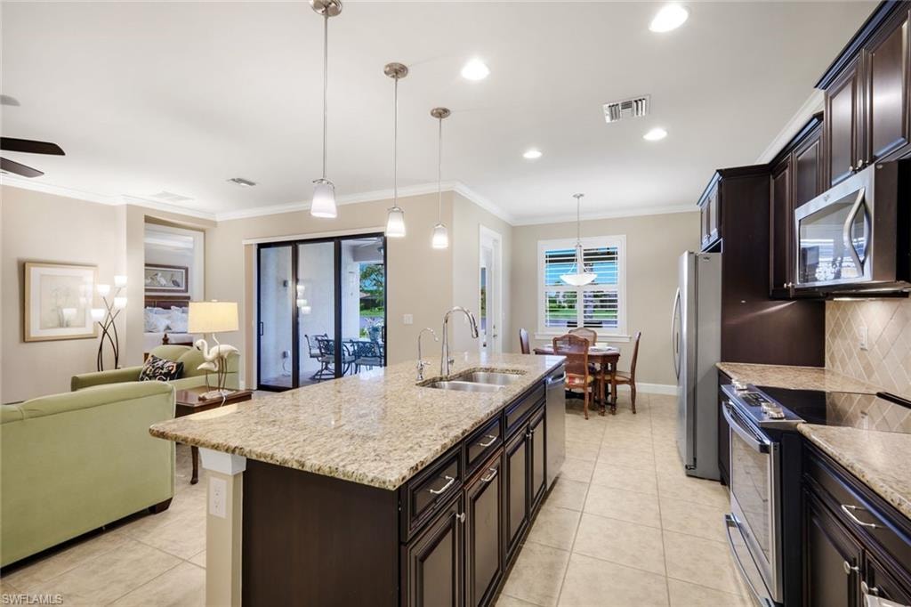 Kitchen island with granite countertop, stainless steel appliances, dark wood-finish cabinetry, and tile flooring