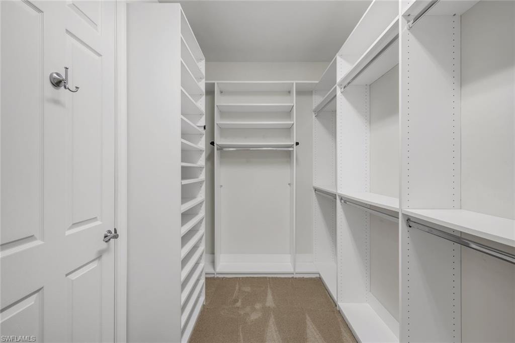 Walk-in closet with built-in shelving, multiple hanging rods, and neutral-toned carpeting