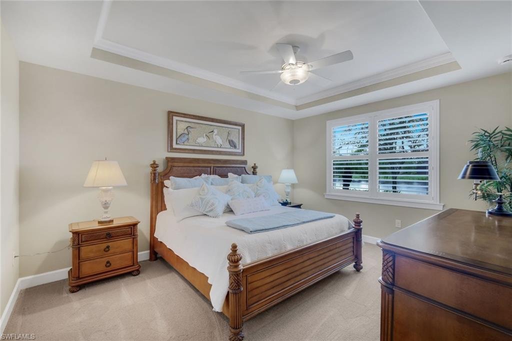 Tray ceiling, ceiling fan, window with white plantation shutters, carpeted flooring, and crown molding
