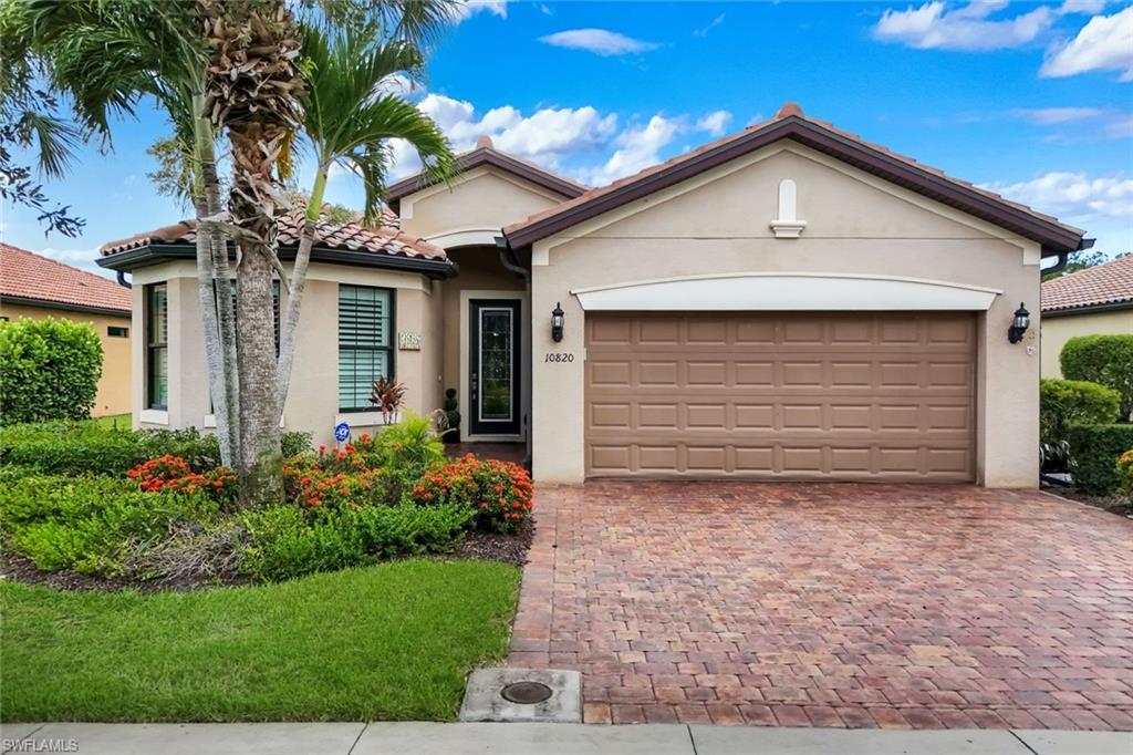 Stucco exterior with a tiled roof, bay window, paver driveway, and an attached garage