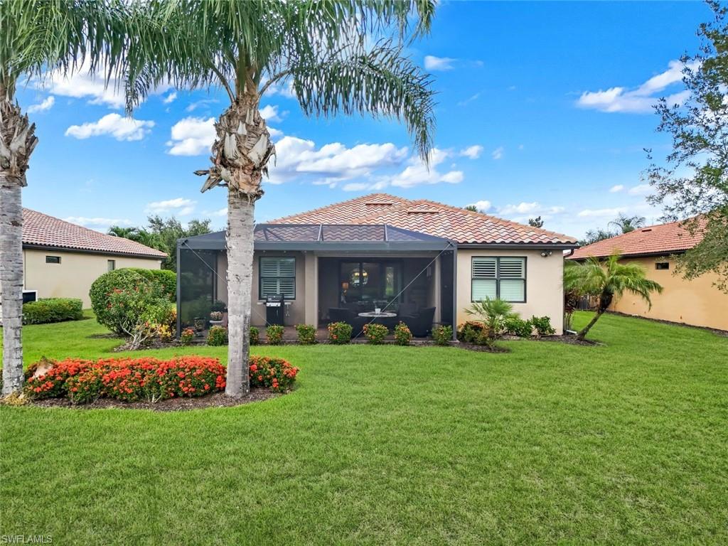 Expansive rear yard with a screened lanai, manicured lawn, lush landscaping, and mature palm trees