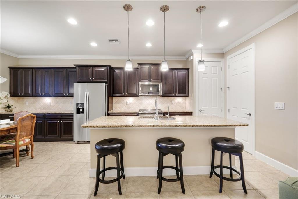 Kitchen featuring dark wood cabinetry, a light-toned tile backsplash, stainless steel appliances, and a central island with a light-toned countertop
