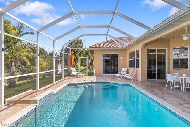 Screened-in outdoor living space featuring a freeform pool with blue mosaic tile accents, a spacious paver patio, a terracotta tile roofline, and multiple sliding glass doors providing interior access