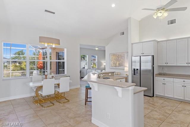 Bright, open kitchen featuring a large center island with seating, stainless steel appliances, white cabinetry, and neutral tile flooring