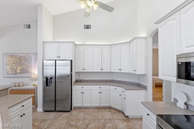 Spacious kitchen featuring white cabinetry with shaker-style doors, stainless steel side-by-side refrigerator with ice and water dispensers, dual wall ovens, and a curved island with seating