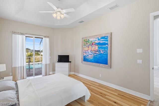 Bright master bedroom featuring hardwood flooring, ceiling fan with integrated lighting, and sliding glass doors opening to a private balcony