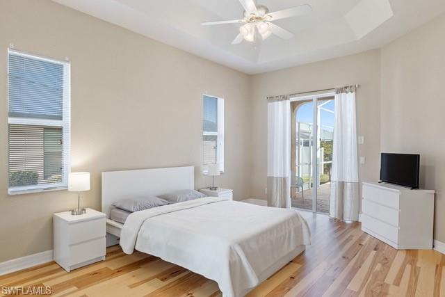 Bright and airy bedroom featuring hardwood flooring, a ceiling fan with integrated lighting, and abundant natural light from multiple windows