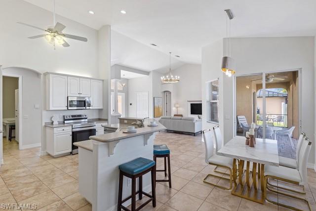Open-concept kitchen and living area featuring white cabinetry, stainless steel appliances, a large center island with seating, tile flooring, recessed lighting, ceiling fans, and pendant fixtures