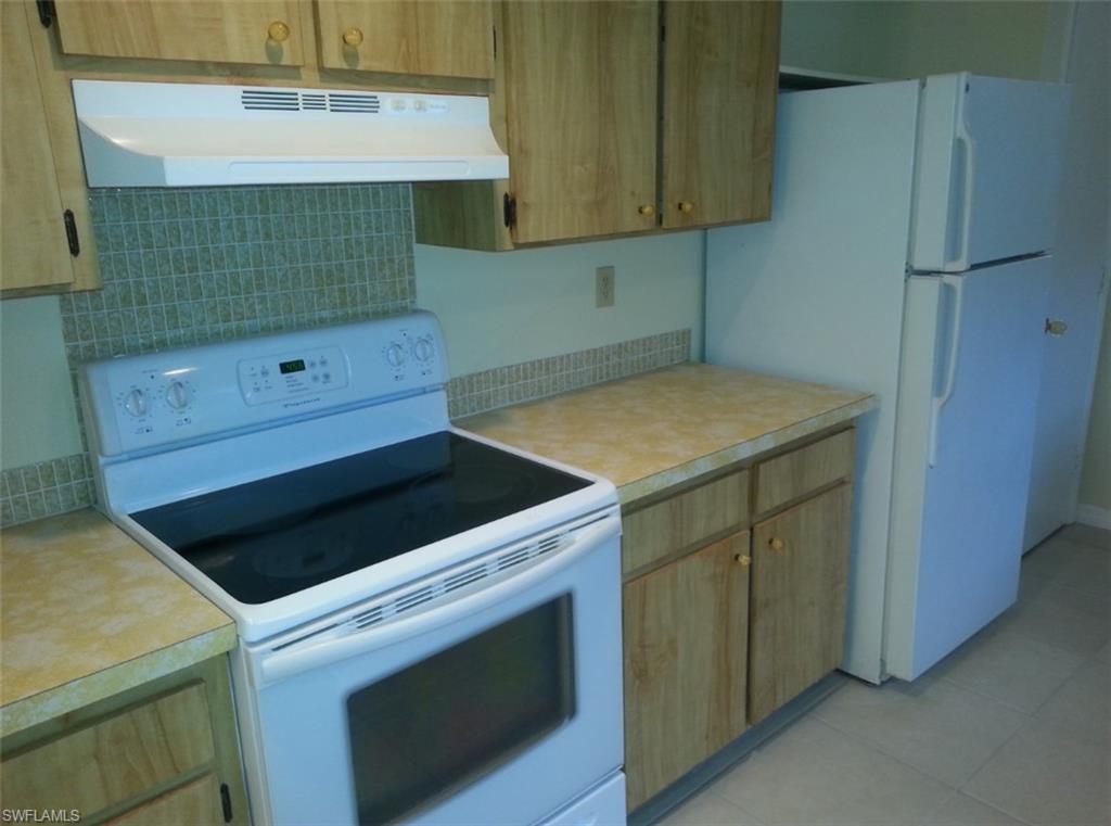 Kitchen featuring decorative backsplash, light tile patterned floors, white appliances, and exhaust hood